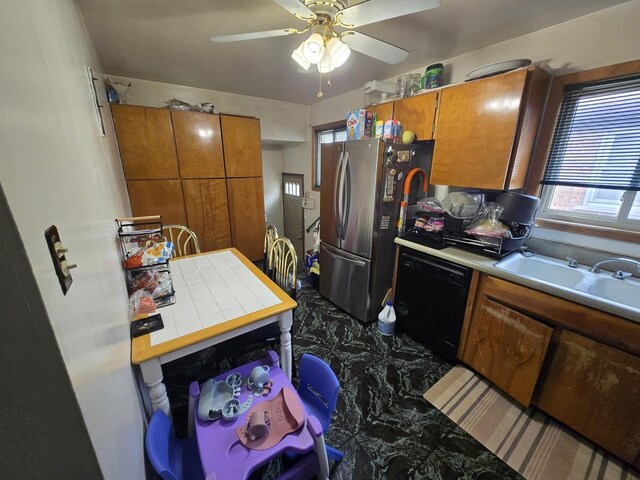 kitchen featuring brown cabinetry, freestanding refrigerator, ceiling fan, a sink, and dishwasher