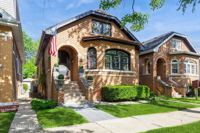 tudor-style house featuring brick siding, stairway, and a front lawn