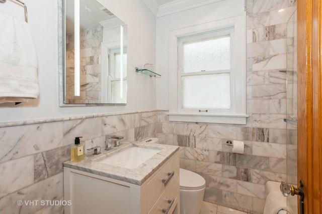 bathroom with tile walls, ornamental molding, toilet, vanity, and wainscoting