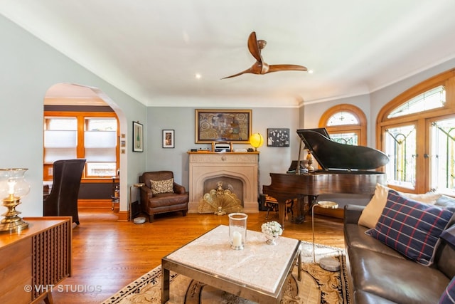 living room featuring arched walkways, a ceiling fan, wood finished floors, baseboards, and ornamental molding
