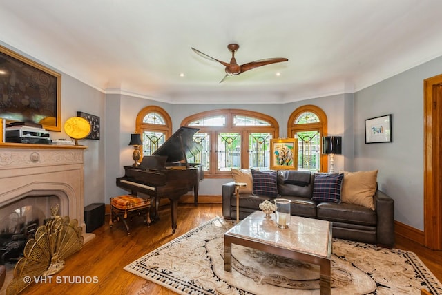living room with a ceiling fan, wood finished floors, baseboards, a fireplace, and crown molding