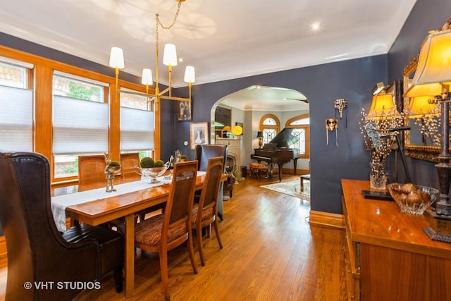 dining area with arched walkways, wood finished floors, a chandelier, and baseboards