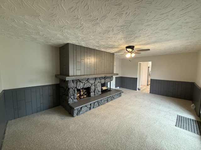 405 9th St, Mazon, IL 60444 - unfurnished living room with a ceiling fan, a stone fireplace, wood walls, a wainscoted wall, and carpet