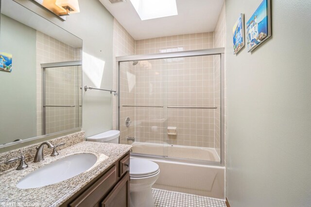 full bathroom featuring a skylight, tile patterned floors, vanity, combined bath / shower with glass door, and toilet
