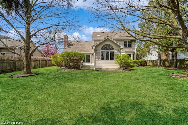 back of house with a fenced backyard, a chimney, and a yard