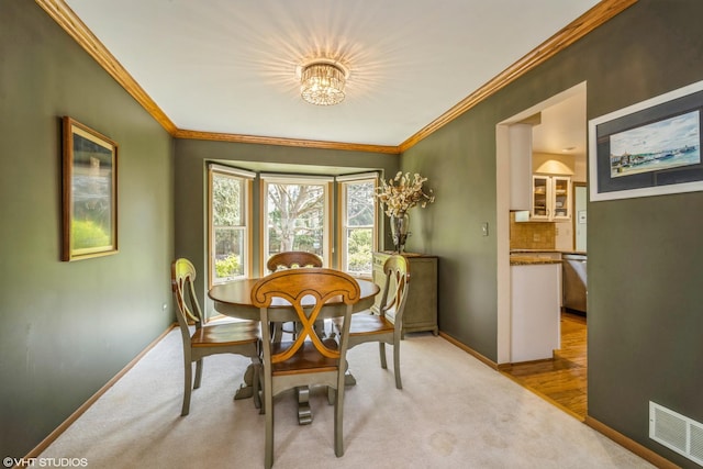 carpeted dining area with crown molding, baseboards, visible vents, and an inviting chandelier