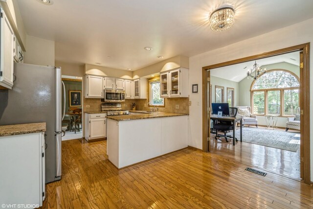 kitchen featuring white cabinets, wood-type flooring, a notable chandelier, glass insert cabinets, and stainless steel appliances