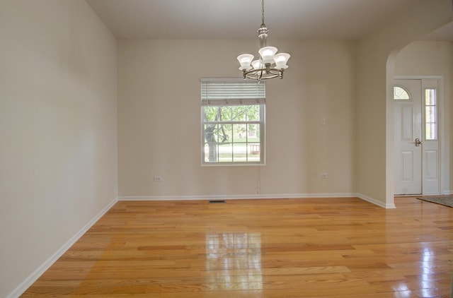 1120 Redwood Ln, Minooka, IL 60447 - empty room featuring arched walkways, light wood finished floors, a chandelier, and a wealth of natural light
