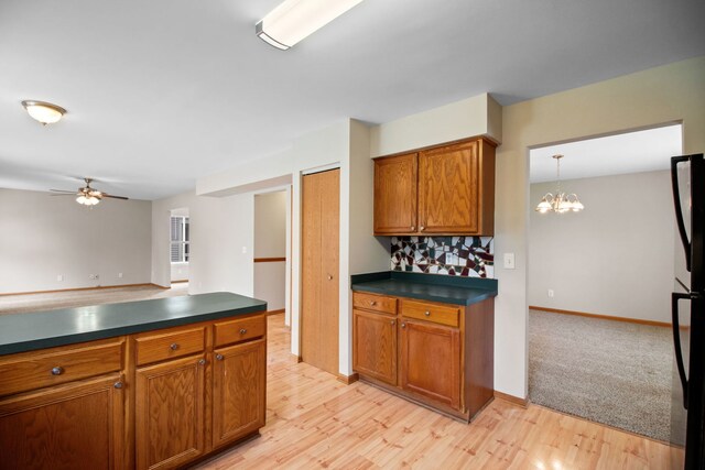 kitchen with dark countertops, brown cabinetry, ceiling fan with notable chandelier, and light wood-style flooring