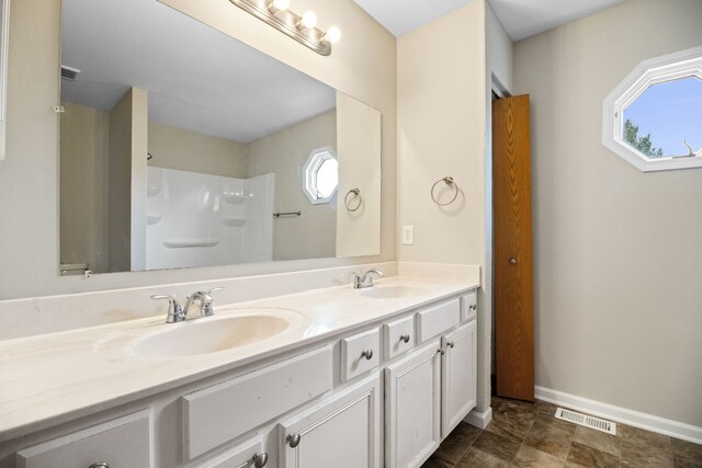 bathroom with a sink, walk in shower, double vanity, and visible vents