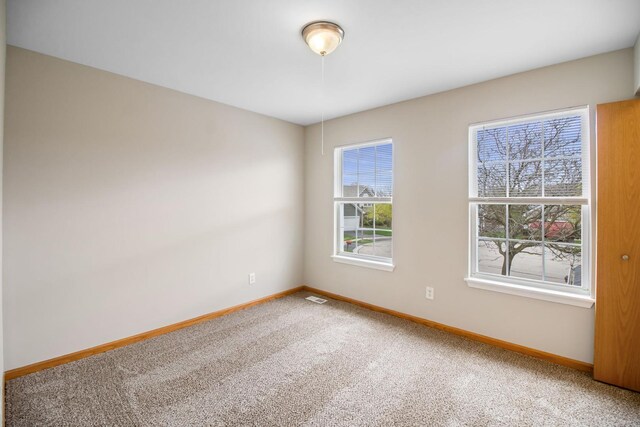 carpeted spare room featuring baseboards and visible vents