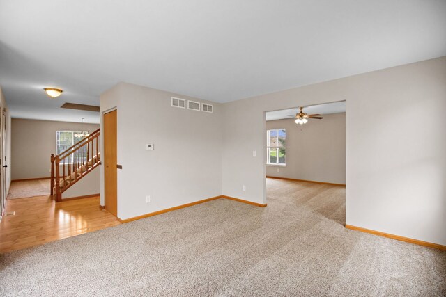 spare room featuring baseboards, light carpet, a ceiling fan, and stairs