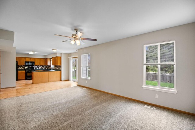 unfurnished living room with visible vents, a ceiling fan, baseboards, and light carpet