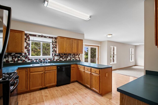 kitchen featuring a peninsula, dark countertops, light wood-type flooring, a sink, and black appliances