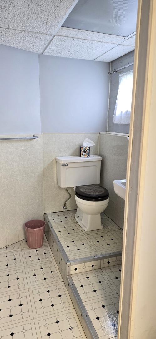 bathroom with wainscoting, toilet, tile walls, a drop ceiling, and tile patterned floors