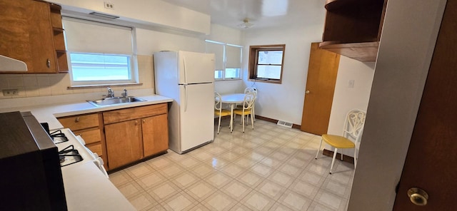 kitchen featuring brown cabinetry, a sink, light countertops, freestanding refrigerator, and light floors