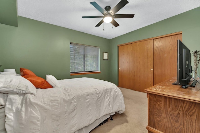 bedroom with a ceiling fan, a textured ceiling, light colored carpet, and a closet