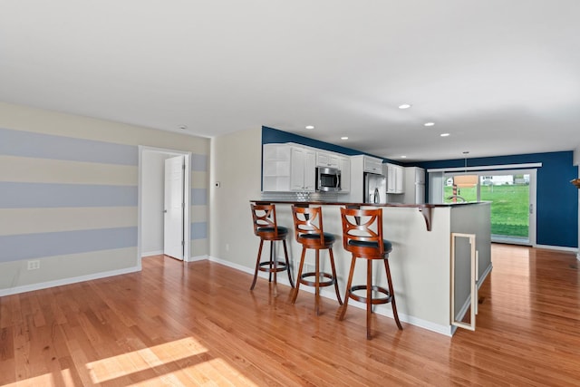 kitchen featuring dark countertops, a breakfast bar area, light wood-type flooring, white cabinetry, and stainless steel appliances