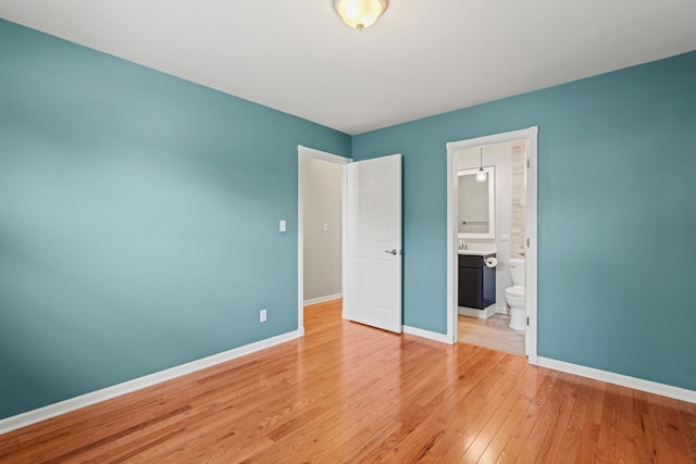 unfurnished bedroom featuring baseboards, ensuite bathroom, and light wood-style floors