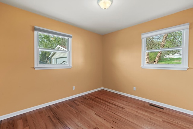 unfurnished room with baseboards, wood finished floors, and visible vents