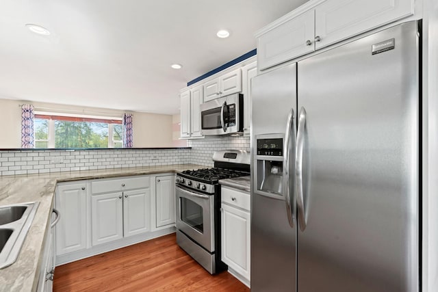 kitchen featuring decorative backsplash, recessed lighting, white cabinetry, light wood-style flooring, and appliances with stainless steel finishes