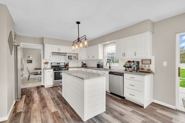 kitchen featuring decorative backsplash, appliances with stainless steel finishes, wood finished floors, baseboards, and under cabinet range hood