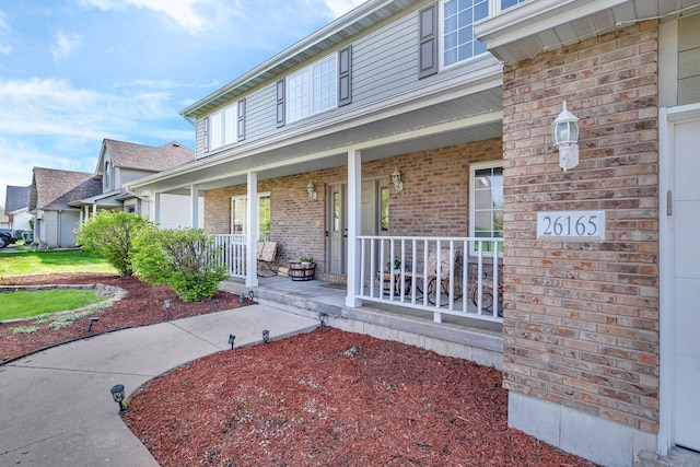 view of exterior entry with brick siding and covered porch