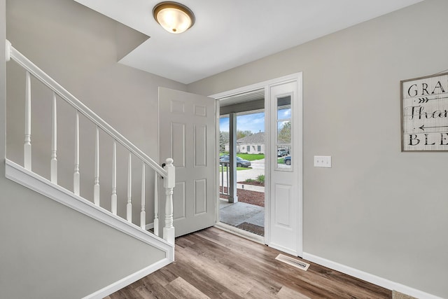 entryway with stairs, baseboards, visible vents, and wood finished floors