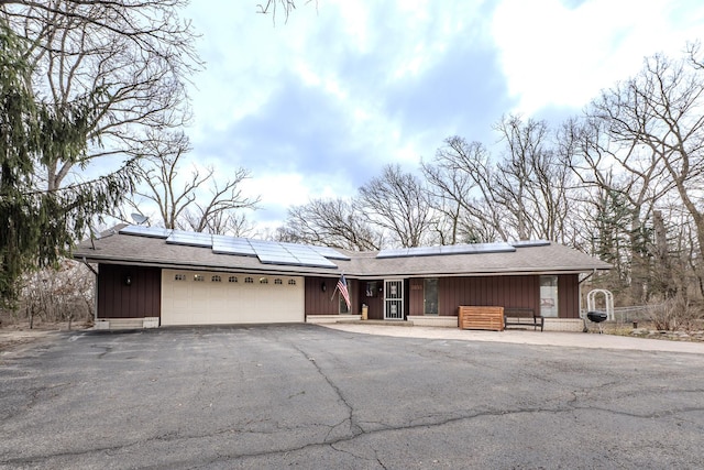 view of front of property featuring a garage, a shingled roof, board and batten siding, driveway, and solar panels