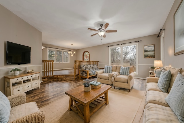 living area with baseboards, wood finished floors, and ceiling fan with notable chandelier