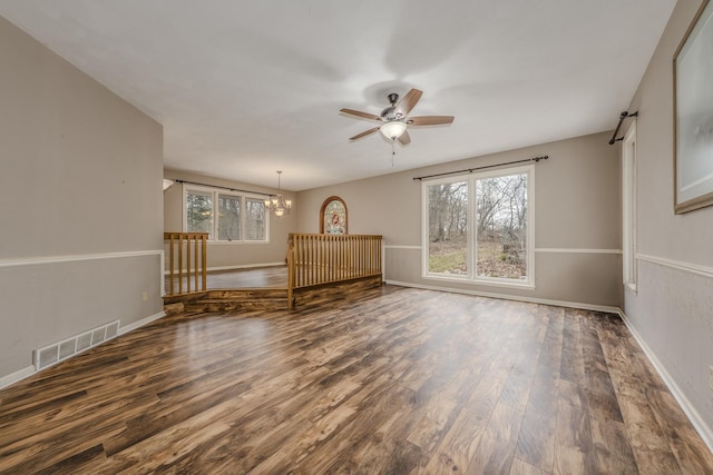 empty room featuring baseboards, ceiling fan with notable chandelier, wood finished floors, and visible vents