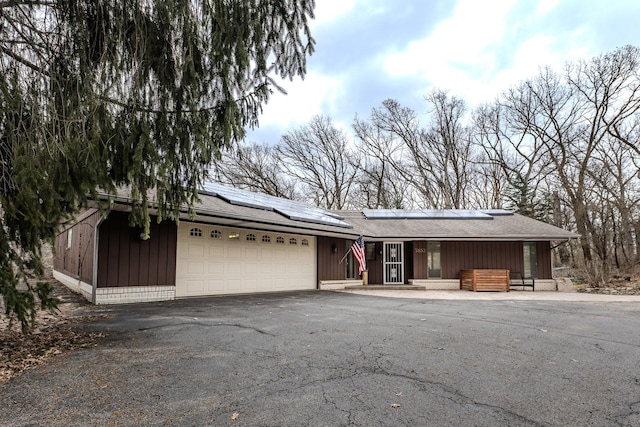 view of front of house featuring a porch, driveway, solar panels, a garage, and a shingled roof