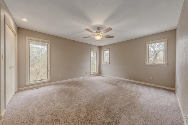 unfurnished room with baseboards, light colored carpet, a healthy amount of sunlight, and ceiling fan