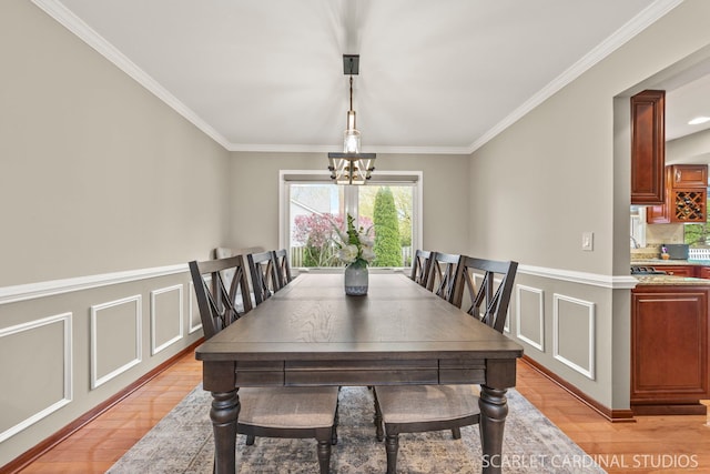 dining room featuring a decorative wall, a chandelier, crown molding, and light wood-style flooring