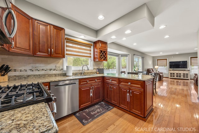 kitchen with a sink, a peninsula, dishwasher, light wood-style flooring, and decorative backsplash