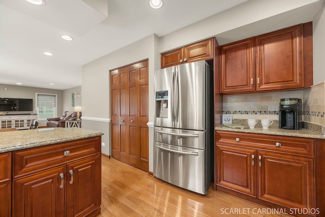 kitchen featuring light wood finished floors, stainless steel fridge with ice dispenser, tasteful backsplash, and light stone countertops