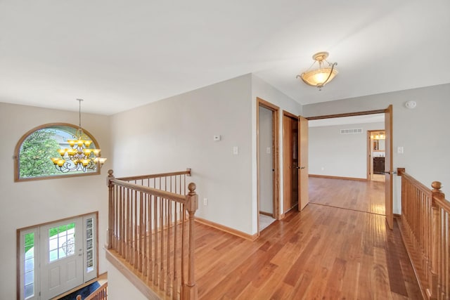 hallway with visible vents, baseboards, light wood finished floors, an upstairs landing, and an inviting chandelier