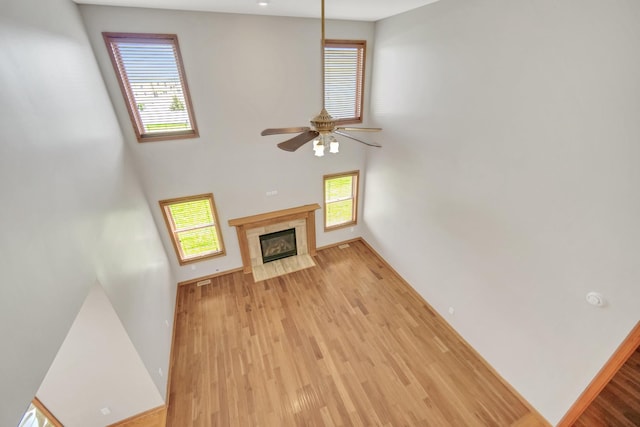 unfurnished living room with a ceiling fan, a towering ceiling, wood finished floors, baseboards, and a premium fireplace
