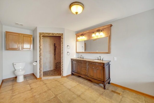 bathroom featuring toilet, baseboards, a tile shower, and a sink