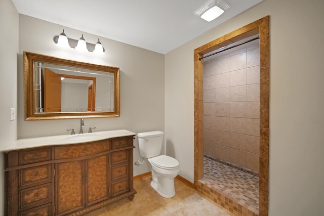 bathroom featuring tile patterned flooring, vanity, toilet, baseboards, and tiled shower