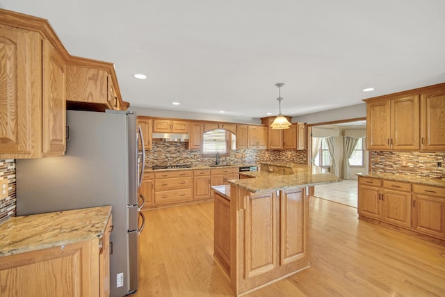 kitchen featuring decorative backsplash, appliances with stainless steel finishes, a sink, under cabinet range hood, and light wood-style flooring