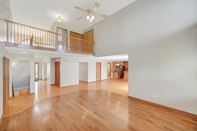 unfurnished living room with light wood-style floors, a ceiling fan, a towering ceiling, and visible vents