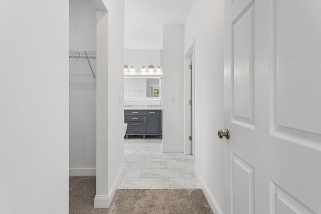 hall with baseboards, light marble finish floors, and a sink