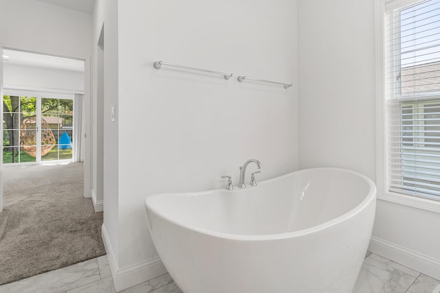 bathroom featuring marble finish floors, baseboards, and a freestanding tub