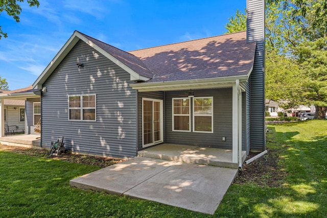 back of property featuring a lawn, a chimney, a patio area, and a shingled roof