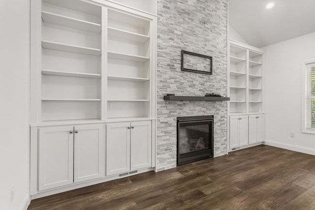 unfurnished living room with a stone fireplace, baseboards, dark wood finished floors, built in shelves, and lofted ceiling