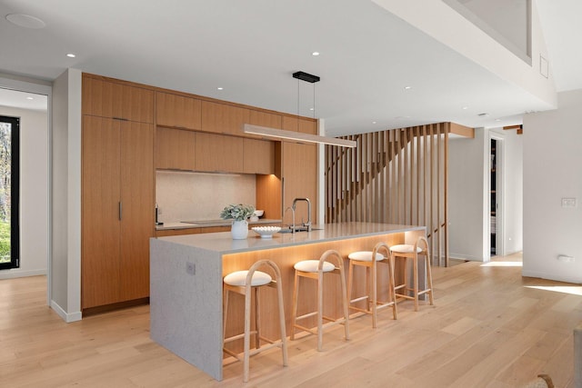 kitchen with light wood-style floors, a large island with sink, light countertops, a sink, and recessed lighting