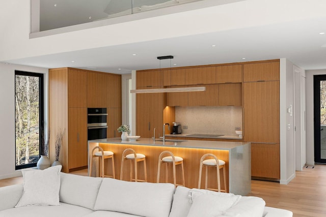 kitchen with a sink, double oven, modern cabinets, light wood-type flooring, and backsplash