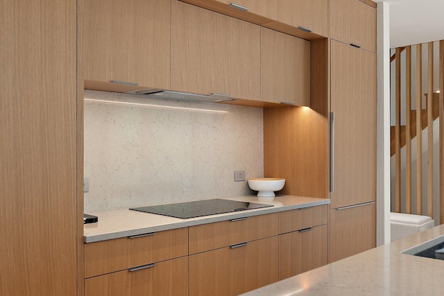 kitchen featuring black electric stovetop, light brown cabinetry, modern cabinets, and light stone countertops