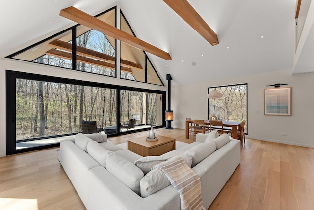 living area featuring high vaulted ceiling, beamed ceiling, light wood-style flooring, and baseboards